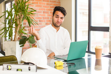 young hispanic man making capice or money gesture, telling you to pay your debts!. architect concept