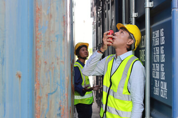 Foreman using smart mobile phone and walkie talkie radio control loading containers box.. Worker with safety hat work at container cargo site and checking industrial container cargo freight ship.