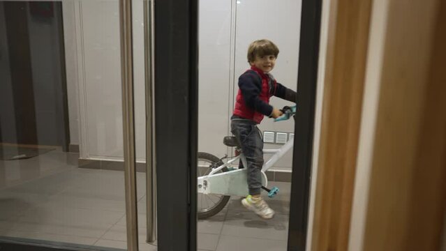 Child arriving home with bicycle. Little boy entering front door of building with bike