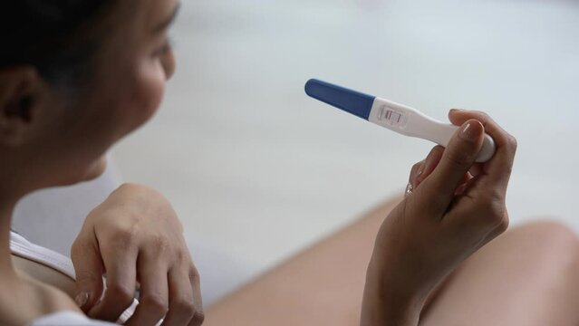 Young Asian woman feeling happy while looking at the positive results of a pregnancy test.