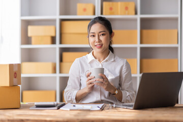 Asian SME business woman using laptop computer Phone checking customer order online shipping boxes at home. Starting Small business entrepreneur SME freelance. Online business, Work at home concept.