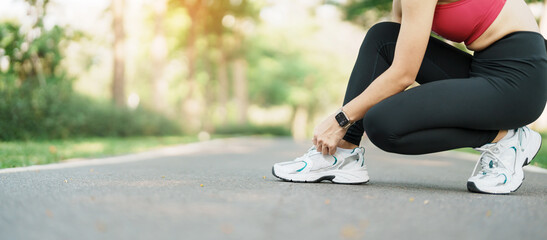 Naklejka premium Young athlete woman tying running shoes in the park outdoor, female runner ready for jogging on the road outside, asian Fitness walking and exercise on footpath in morning. wellness and sport concepts