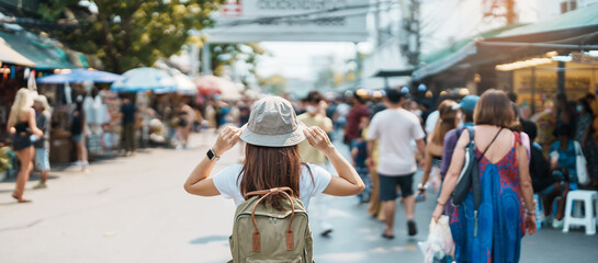 woman traveler visiting in Bangkok, Tourist with backpack and hat sightseeing in Chatuchak Weekend Market, landmark and popular attractions in Bangkok, Thailand. Travel in Southeast Asia concept - obrazy, fototapety, plakaty