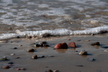Colorful sea pebbles on the shore of the Baltic Sea on the background of an incoming wave, Curonian spit, Kaliningrad region, Russia
