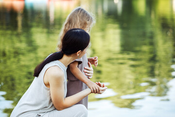A young mother and her five-year-old daughter are standing on the bridge by the lake and looking at the water.