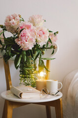 Still life details in home interior of living room. Open book with glasses, cup coffee and bouquet white pink peonies flowers. Read and rest. Cozy home