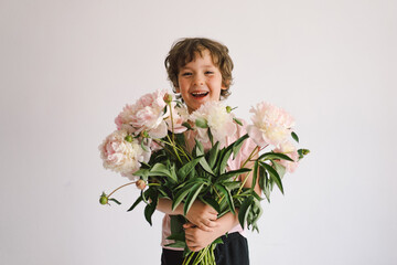 Cheerful happy child with Peonys bouquet. Smiling little boy on white background. Mother's Day. Love and romantic concept