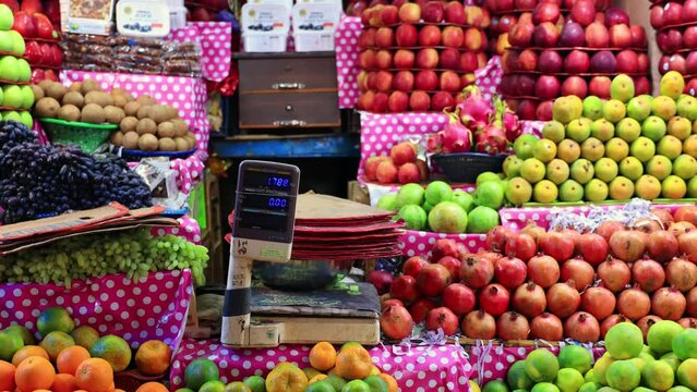 Multiple bright colored fresh fruits for sale in a Indian Fresh Fruit Market. Mysuru, Karnataka, India. A weighing scale at the center of the shop.