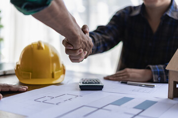 Yellow hard hat on table and house design print design with construction team handshake greeting...
