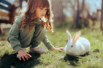 Little Girl Playing with her Rabbit Outside on the Grass. Toddler child feeding a pet bunny having...