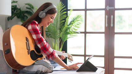 Fototapeta na wymiar Guitar and singer concept, Young asian woman playing acoustic guitar while learning music on tablet