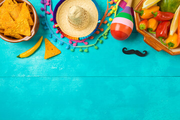 Cinco de Mayo holiday celebration with nacho chips, peppers, maracas and mexican party decorations on blue wooden background. Top view, flat lay - 585620254