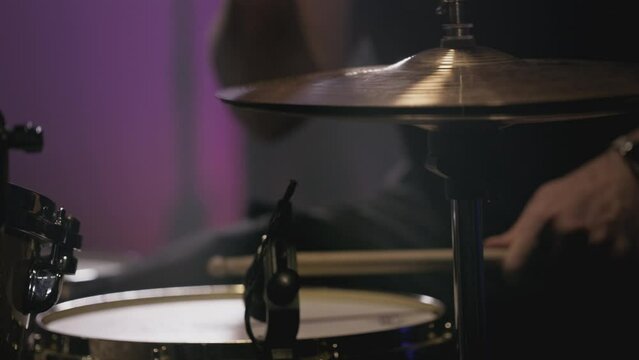 a young attractive guy plays a drum kit. Strikes a cymbal, rehearses. Performance of a rock band, hobby. A man is learning music. Male professional holds drumsticks in hands. Drum set in slow motion