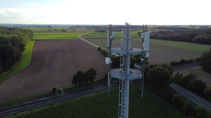 Ansbach, Germany / Bavaria - August 22, 2020: Wide Area Network (WAN) 3G 4G 5G LTE mobile radio broadband transceiver communications tower with, corn field, building , and view from above.