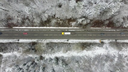 Munich, Germany Bavaria - April 4, 2022: Striped paved winter road winding through the snowy forest trees with a bike path, yellow truck, and cars. Image taken from a drone at 100m altitude.