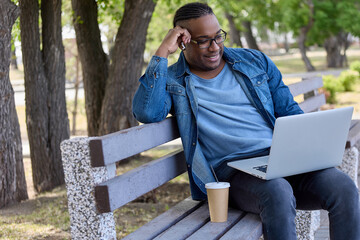 Popular Afro blogger reads a news feed on the Internet sitting in a park with a glass of delicious coffee. African-American pretty student with glasses prepares for an exam in nature in silence