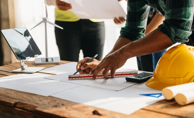 three colleagues discussing data working and tablet, laptop with on on architectural project at construction site at desk in office.