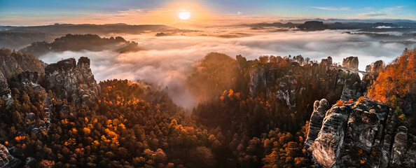 Saxon, Germany - Aerial panoramic view of the beautiful Saxon Switzerland National Park near Dresden on a foggy autumn morning with Bastei bridge, rock formation and golden autumn foliage at sunrise