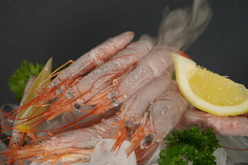 Frozen red tiger prawns on ice cubes with lemon bites composition, close up