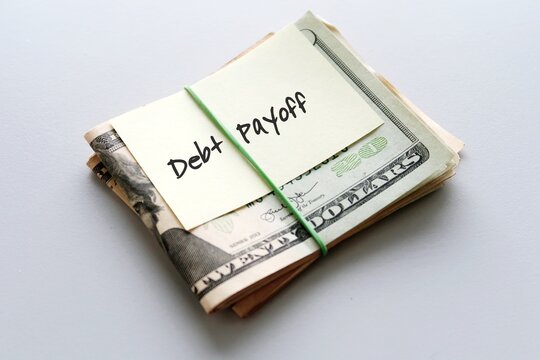 Dollars cash money in rubber band with text written note  DEBT PAYOFF , on copy space background - concept of financial planning to save money for purpose of getting out of debt