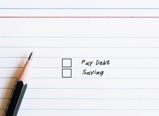 Paper notebook sheet and a pencil , with two choices checklists to choose between DEBT and SAVING. Concept of financial decision making