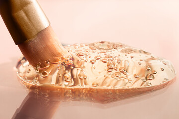 Transparent cosmetic texture with bubbles macro. Hyaluronic acid, serum, soap with a cosmetic brush on a beige background.