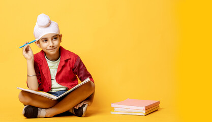 indian Sikh kid with book sitting on floor and thinking creative