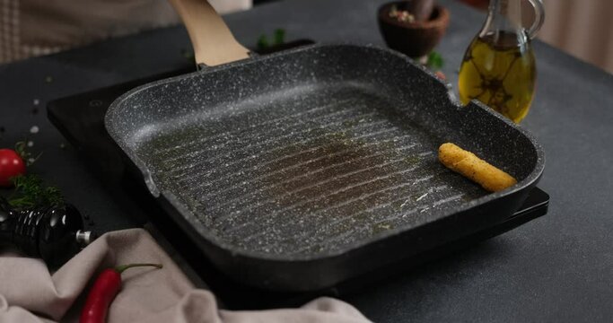 Woman puts cheese sticks into hot oiled grill frying pan