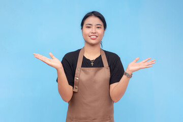 A young lovely female barista of asian descent wearing a brown apron and black shirt presenting something with both hands. Against a light blue background.