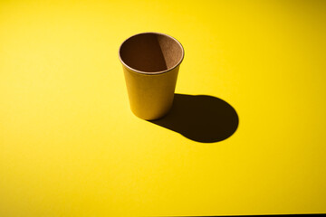 Cardboard coffee cup on yellow background with shadow.