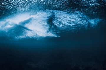 Wave underwater and surfer riding on surfboard in ocean. Underwater crashing wave and surfboard in...