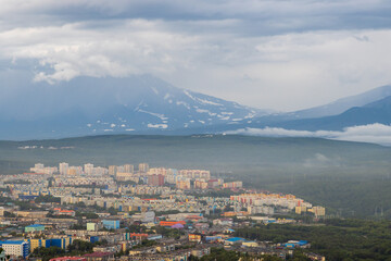 Fototapeta na wymiar Summer cityscape. Top view of the buildings and streets of the city. Residential urban areas. Volcanoes in the distance. Cloudy rainy weather. Petropavlovsk-Kamchatsky, Kamchatka, Far East of Russia.