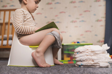 Potty training concept. A three-year-old boy sits on a potty in a children's room among toys and ...