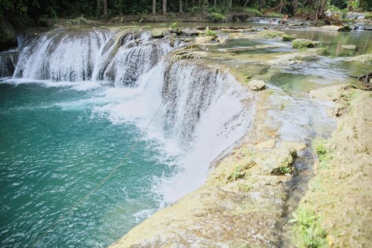The idyllic Cambugahay Waterfalls in Siquijor in the Philippines that flow into a natural pool of water surrounded by the light-lit rainforest.