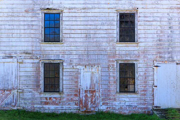 Fototapeta na wymiar Faded white paint on wall, doors, and windows of historic western building