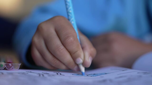 Child hand drawing on paper with blue color pencil. Kid draws Macro Closeup. Creative childhood development