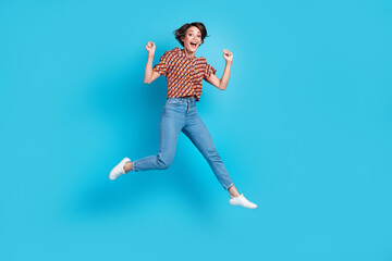 Fototapeta na wymiar Full size portrait of delighted pretty girl jumping raise fists shout yes hooray isolated on blue color background