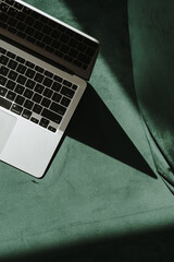 Flatlay laptop computer on green velour sofa with aesthetic sunlight shadows. Minimal work,...