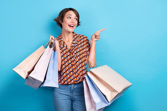 Photo of adorable excited lady dressed print shirt holding shoppers showing looking empty space isolated blue color background