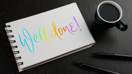 WELL DONE! colorful hand lettering in notebook with cup of coffee and pens on black wooden desk
