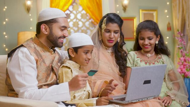 happy indian muslim couple with kids purchasing or shopping online during festival disacount sales using credit card on laptop - concept of e-commerce, festival sale and technology.