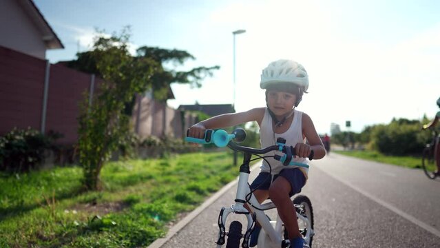 Happy child rides bicycle outside in bike lane in sunny day with flare. Active young boy wearing helmet riding bike outdoors. Sportive kid weekend activity