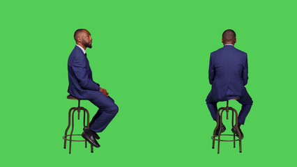 Positive smiling person sitting on chair over greenscreen, looking around and waiting for something. Male entrepreneur wearing office suit over full body green screen backdrop. - Powered by Adobe