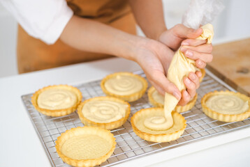Obraz na płótnie Canvas close up hands of Small business entrepreneur asian woman bakery shop making fruit tart. Female Baker Using Piping Bag to Decorate fruit tart with cream cheese on white kitchen counter.