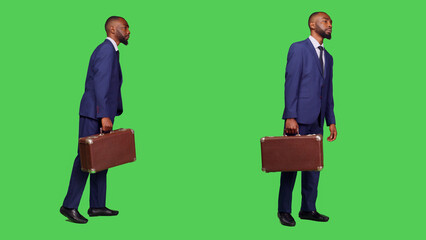 Young manager holding suitcase at company workplace, standing in studio over full body green screen backdrop. Startup worker wearing business suit and carrying briefcase luggage on camera.