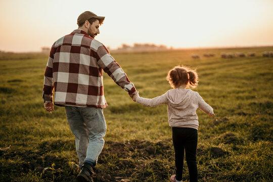 Rear view of a family on holiday vacation. Smiling father and little daughter holding hands and walking together on the meadow field. Parent with cute child girl relax and enjoy an outdoor lifestyle.