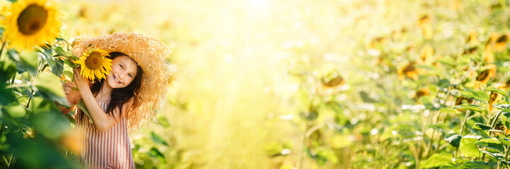 Little happy little girl playing enjoying sunflower flowers on sunny summer day field. Spring and summer background banner. Horizontal photo banner for website header design. - obrazy, fototapety, plakaty