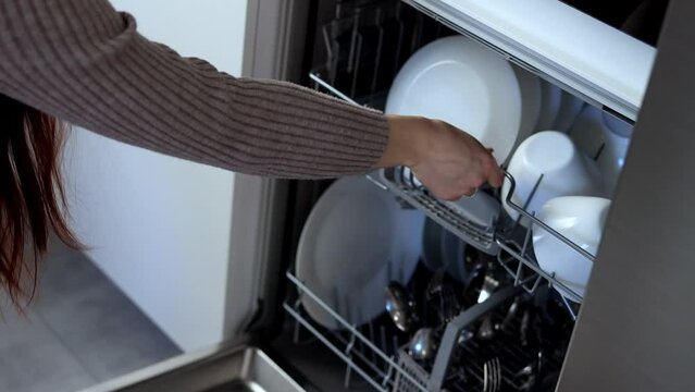 A young woman closes the dishwasher with white dishes. Build into the kitchen. Modern home kitchen. Housework