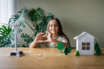 Girl making heart gesture sitting at table with with wind turbine model