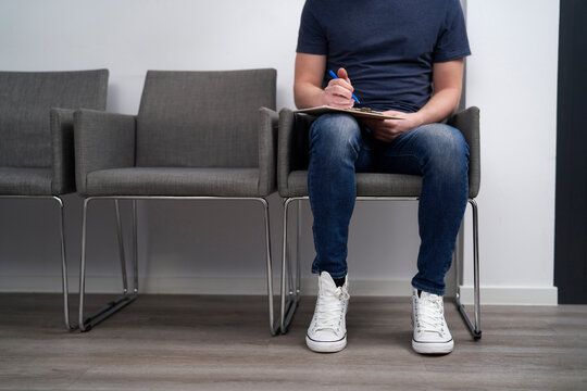 Man Filling Form Sitting On Chair In Waiting Room